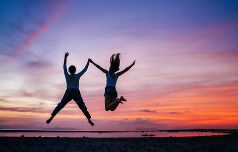 Two running and jumping girlfriends on the sunset sea beach. Han